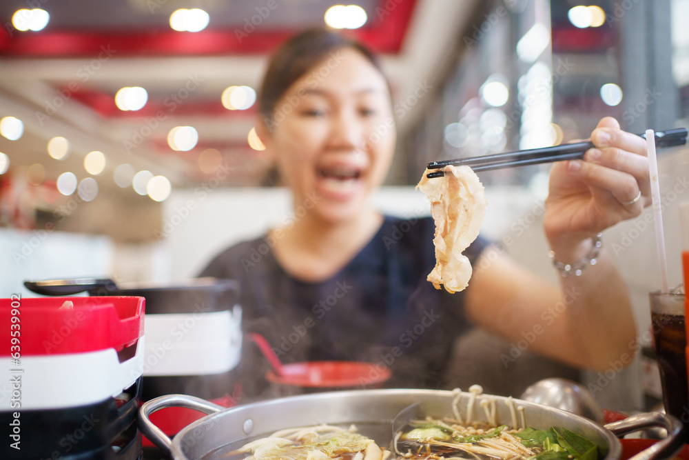 Happy - cheerful Asian fat woman enjoy eating a traditional Asian Hotpot or Sukiyaki in the Asian Hotpot restaurant.