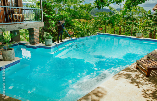 Man cleaning a beautiful swimming pool with suction hose. Pool maintenance and cleaning with vacuum hose. Swimming pool cleaning and maintenance service