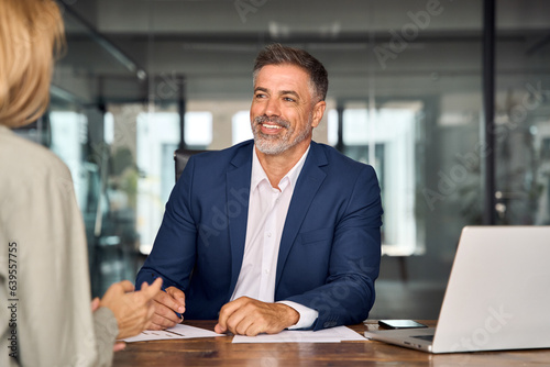 Lawyer or real estate agent make consultation for client. Mature Latin business man and European business woman discussing project on laptop sitting at table in office. Business people work together.