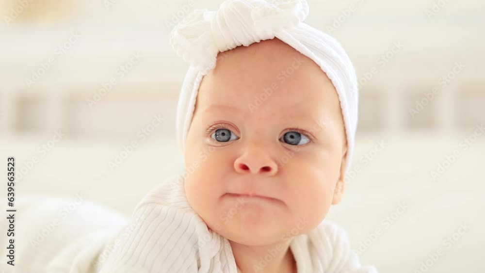 baby girl with blue eyes portrait close-up, happy little baby lying in a bright bedroom in a white bodysuit baby girl with blue eyes portrait close-up, happy little baby lying in a bright bedroom in a white bodysuit
