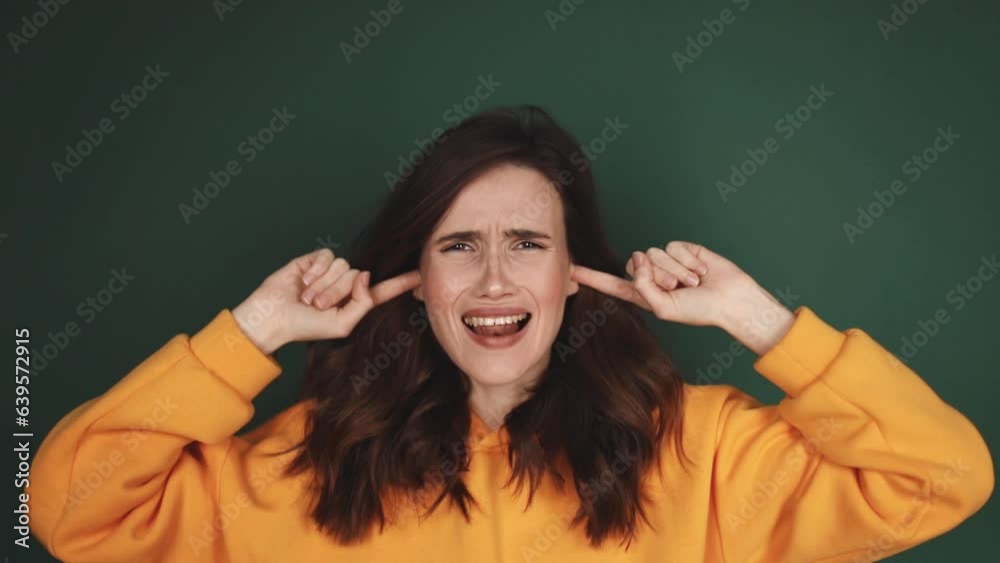 Carefree curly woman in yellow hoody covering her ears and does not want to listen to anything over green background. Girl with cover ears says la la la. Carefree curly woman in yellow hoody covering her ears and does not want to listen to anything over green background. Girl with cover ears says la la la.