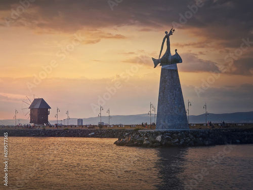 Statue of Saint Nicholas the patron of sailors, in the old town of Nessebar, Burgas, Bulgaria. Sunset scene at the coastline with a beautiful view to the big monument and the mill near the harbor