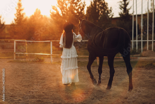 Woman in white dress and black hat with her horse at sunset outdoors ranch