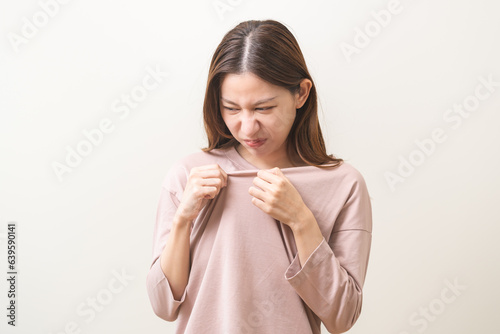 Bad smelling, deodorant asian young woman smell stink, breathing nose smelly on shirt dirty stinky laundry, disgusting from clothes after washed, smelly armpit underarm Medical health, skin body care. photo