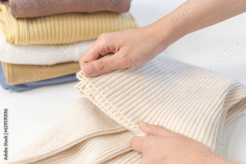 Housewife, asian young woman hand in many folding freshly shirts, sweaters or dress on desk, table after washing clean clothes and drying, making household working in room at home. Laundry and maid.