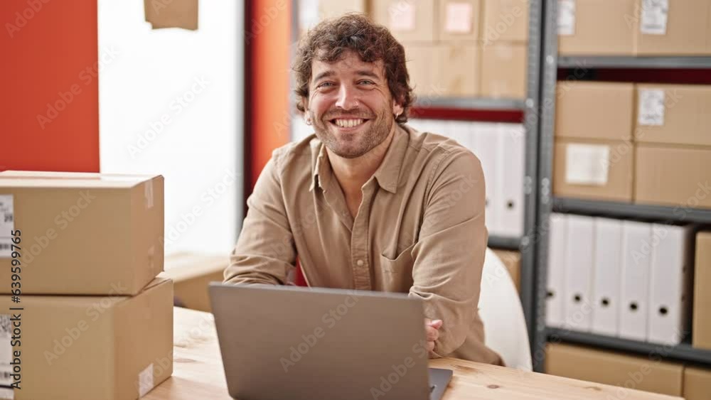 Young hispanic man ecommerce business worker sitting on table smiling at office Young hispanic man ecommerce business worker sitting on table smiling at office