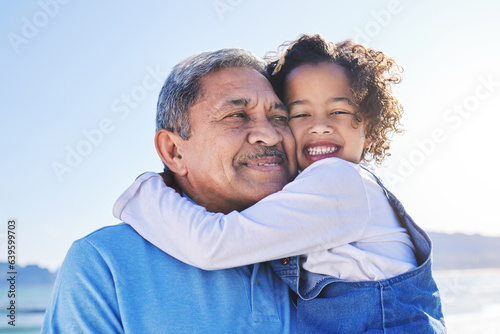 Grandfather, child and happy at the beach for vacation and travel together on outdoor holiday for happiness. Hug, smile and grandparent with kid or young grandchild by the ocean or sea for adventure photo