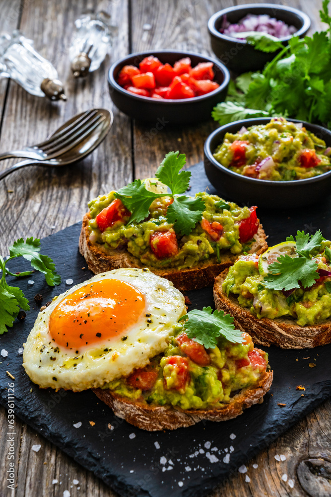 Tasty bruschetta with sunny side up egg, guacamole, tomato, and onion on wooden table
