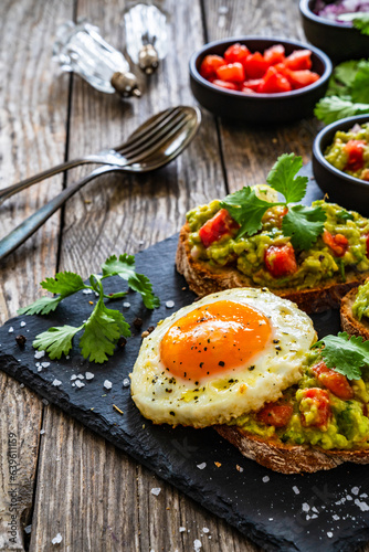 Tasty bruschetta with sunny side up egg, guacamole, tomato, and onion on wooden table 