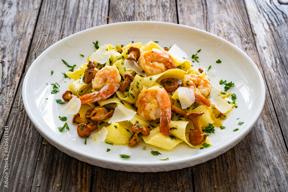 Tagliatelle with chanterelle mushrooms, seared prawns and   Parmigiano Reggiano on wooden table
