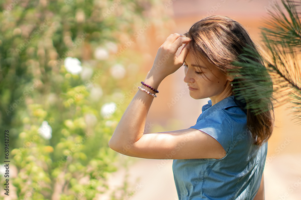 a young white woman stands in profile to the lens, she calmly removes her shiny brown hair from her face with her hand, she is wearing a blue dress, a sunny summer day a young white woman stands in profile to the lens, she calmly removes her shiny brown hair from her face with her hand, she is wearing a blue dress, a sunny summer day