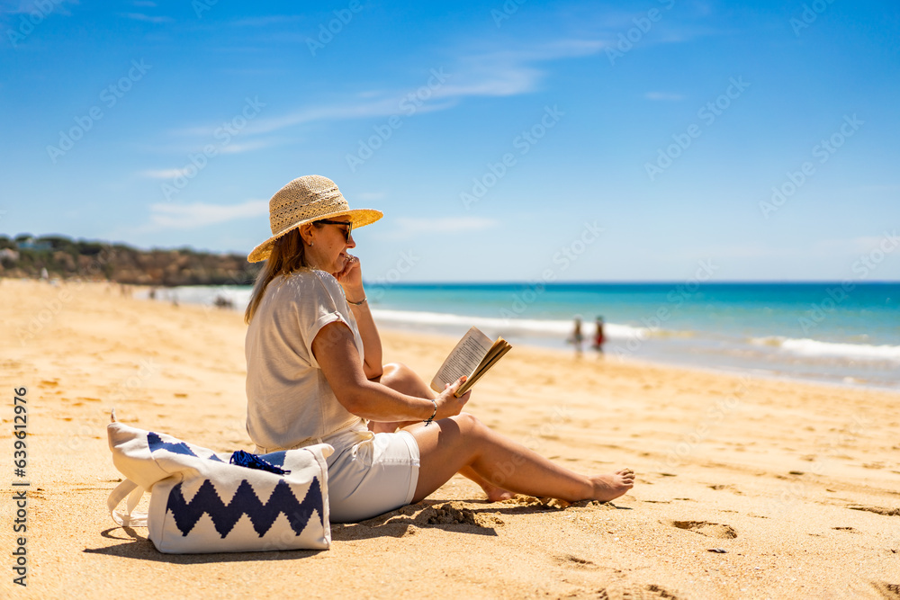 Woman sitting on beach in Alvor, Portugal reading book
