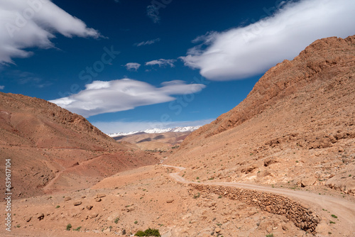 Staubiger Weg in karger Felslandschaft unter blauem Himmel mit Wolken