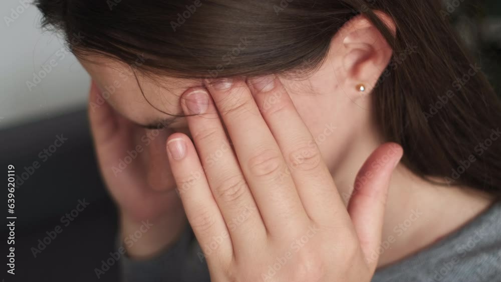 Close up of tired frustrated girl touching head, feeling headache, migraine, sit on couch in living room at home. Depressed young woman coping with loss and trauma. Nervous breakdown, crisis concept Close up of tired frustrated girl touching head, feeling headache, migraine, sit on couch in living room at home. Depressed young woman coping with loss and trauma. Nervous breakdown, crisis concept