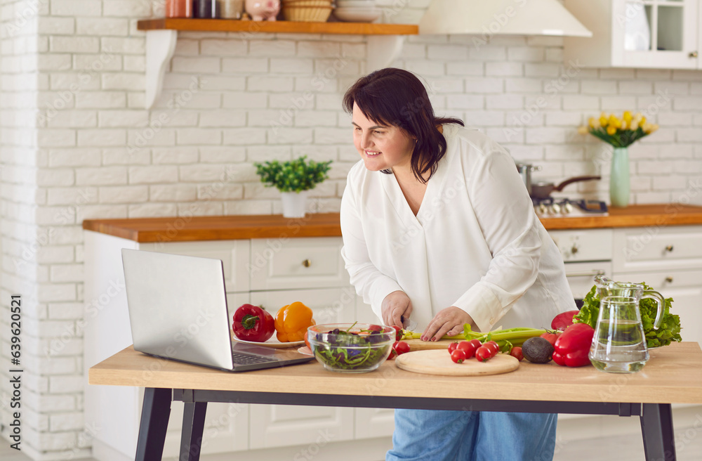 Fat overweight chubby woman learning to cook healthy food, watching master chef class lesson tutorial on modern laptop, making body slimming weightloss diet salad and cutting greens, tomatoes, peppers