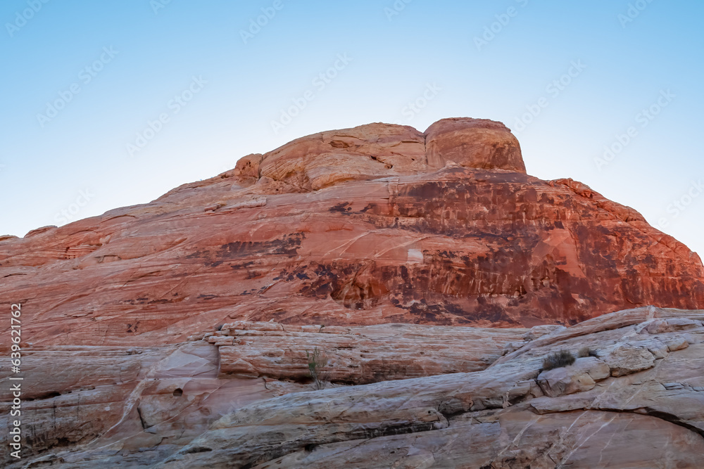 Fototapeta premium Scenic view on wall of striated red and white rock formations along the White Domes Hiking Trail in Valley of Fire State Park in Mojave desert, Nevada, USA. First sunlight touches arid landscape