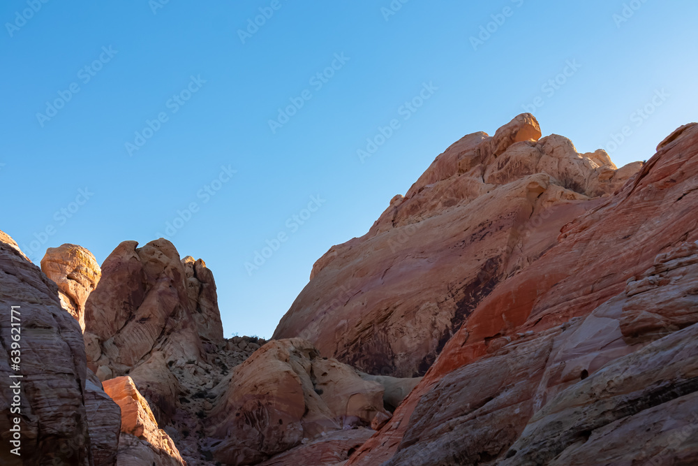 Scenic view on wall of striated red and white rock formations along the White Domes Hiking Trail in Valley of Fire State Park in Mojave desert, Nevada, USA. First sunlight touches arid landscape