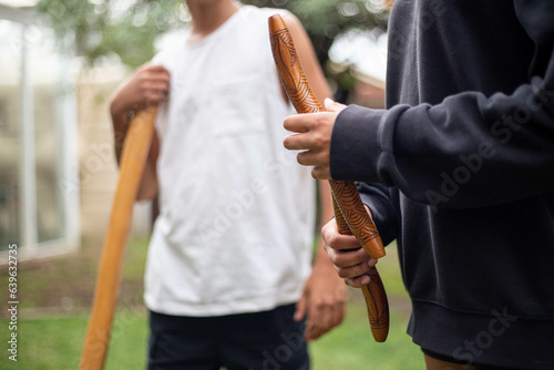 Two people holding Aboriginal instruments in backyard photo