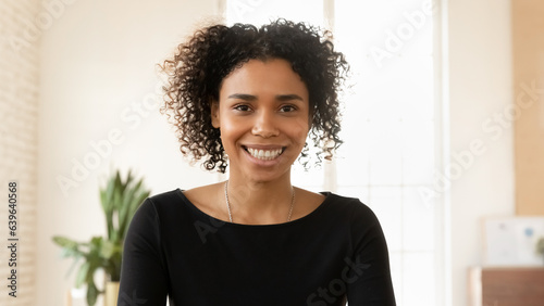 Close up headshot portrait of smiling young african American woman look at camera talk on video call, happy millennial biracial female engaged in webcam virtual conversation, technology concept