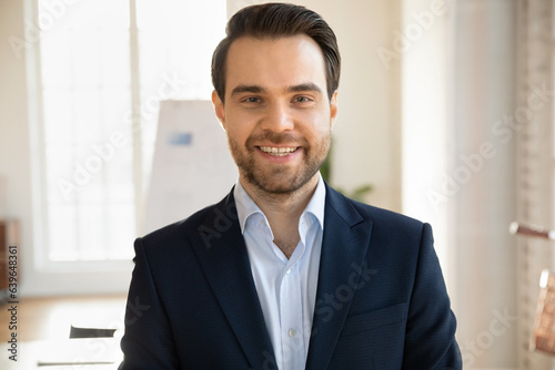 Close up headshot portrait of smiling Caucasian young businessman in formal suit pose in office, profile picture of happy confident male boss or director show success at workplace, leadership concept