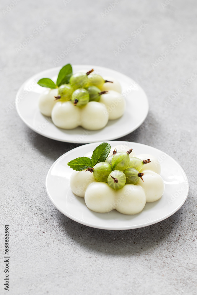 Vegan Gooseberry cream dessert, Panna Cotta in the shape of truffles, decorated with fresh gooseberries. On a plate. Light grey background Vegan Gooseberry cream dessert, Panna Cotta in the shape of truffles, decorated with fresh gooseberries. On a plate. Light grey background