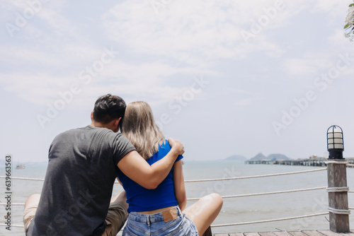 Couple of asian lover hug and hold sitting together looking out to the sea bay.