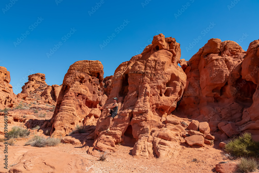 Man at exterior entrance of windstone arch (fire cave) in Valley of Fire State Park, Mojave desert, Nevada, USA. Scenic view of beehive shaped red sandstone rock formations. Barren deserted landscape Man at exterior entrance of windstone arch (fire cave) in Valley of Fire State Park, Mojave desert, Nevada, USA. Scenic view of beehive shaped red sandstone rock formations. Barren deserted landscape