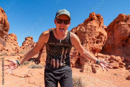 Tourist man screaming out of happiness at entrance of windstone arch (fire cave) in Valley of Fire State Park, Mojave desert, Nevada, USA. Scenic view of beehive shaped red sandstone rock formations photo