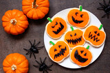 Plate of Halloween jack o lantern cookies. Overhead view with pumpkins on a dark background.