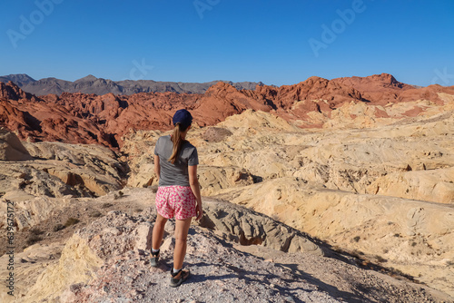 Rear view of woman at Silica Dome viewpoint overlooking the Valley of Fire State Park in Mojave desert, Nevada, USA. Landscape of Aztek sandstone rock formations. Hot temperature in arid vegetation