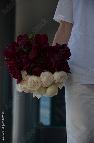 Bouquet of white and burgundy peonies in a male hand