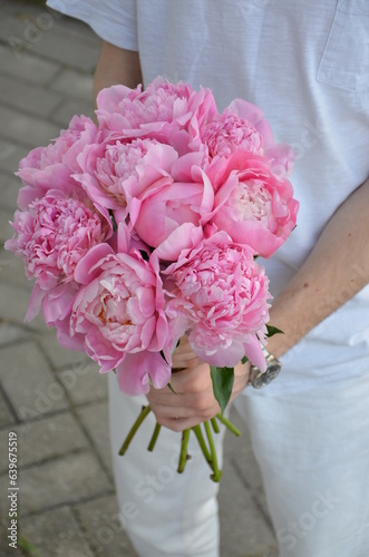 A man holds a bouquet of pink peonies in his hand