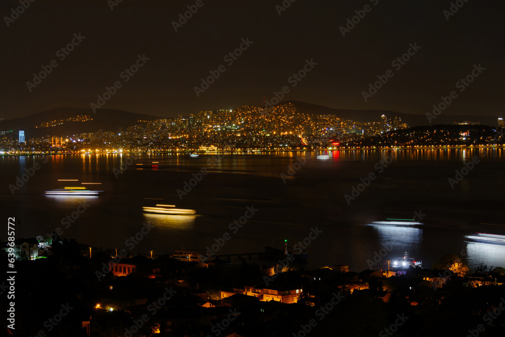 View of city of Istanbul from the Princes Islands at night. Apartment, residential buildings with illuminated windows. Ferries, motor boats light trails