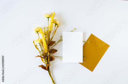 Gold envelope with blank card and flowers on white. Birthday, invitation, holiday concept. Top view, flat lay, mockup.