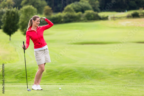 Smiling attractive female golfer shielding eyes while standing on field