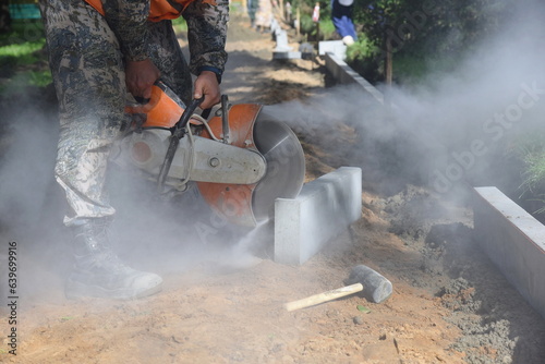 A worker saws a concrete curb with a circular saw, building a pedestrian road.