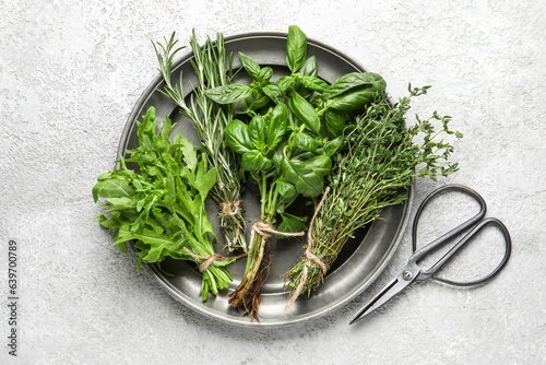 Plate with fresh herbs and scissors on light background