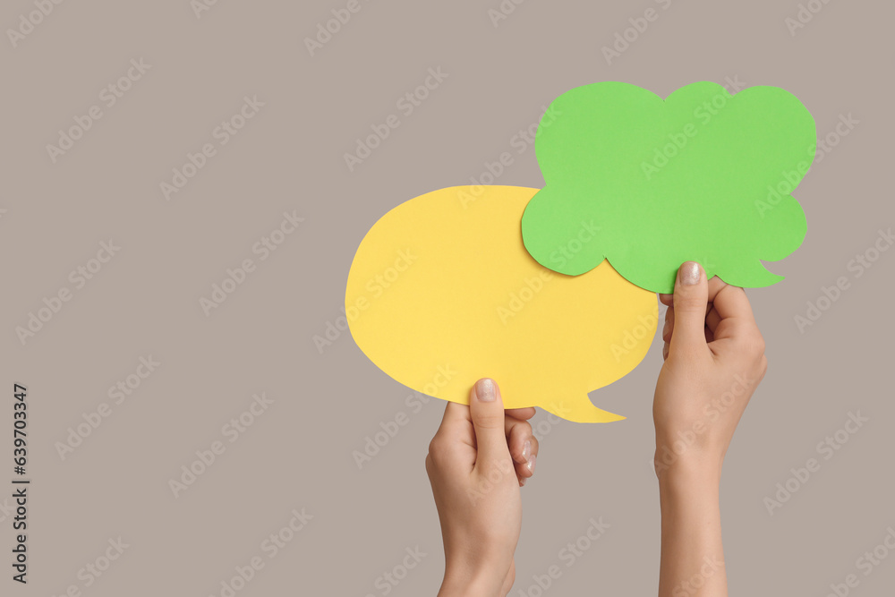 Female hands with speech bubbles on grey background Female hands with speech bubbles on grey background