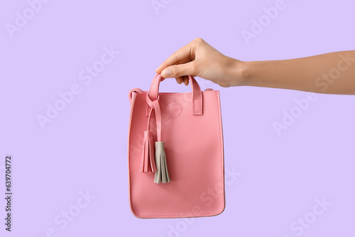 Female hand with stylish pink handbag on lilac background