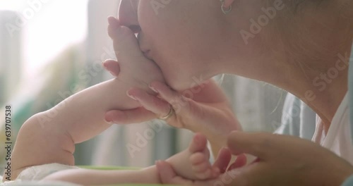 mother kisses her newborn baby feet and toes at home, mommy love, happy motherhood. photo