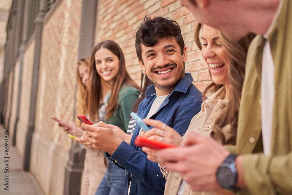 © CarlosBarquero - Side view of multiracial smiling group young generation z leaning brick wall using phones outdoors. Friends having fun together looking at social media. Concept of relationships and new technologies. © CarlosBarquero - Side view of multiracial smiling group young generation z leaning brick wall using phones outdoors. Friends having fun together looking at social media. Concept of relationships and new technologies.