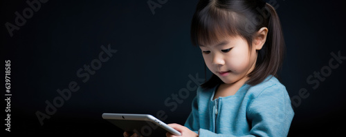 A tablet held in the hands of an Asian elementaryage child actively playing a game that combines fun with learnings in technology. She appears absorbed in her creation. photo