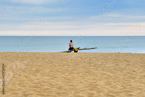 Une femme assise sur un tronc d'arbre face à la mer