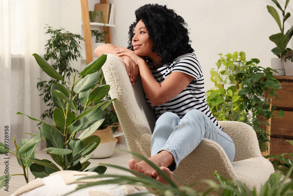 Obraz premium Woman relaxing in armchair surrounded by beautiful houseplants at home