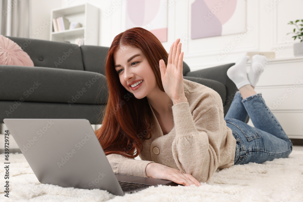 Happy woman with laptop having video chat on rug in living room