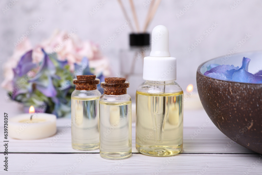 Spa composition. Bottles of essential oil and aromatic water with flowers in bowl on white wooden table, closeup Spa composition. Bottles of essential oil and aromatic water with flowers in bowl on white wooden table, closeup
