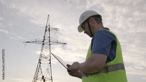 Electrician checkups power transmission lines with tablet standing near tower © Валерий Зотьев