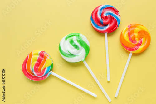 Colorful lollipops, different colored round candy on sticks on yellow background. Flat lay, top view