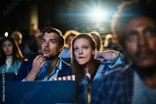 Young couple watching a movie and eating popcorn in a movie theater
