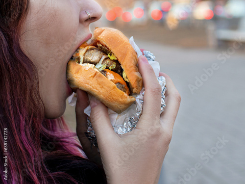 woman biting a burger with 2 cutlets take away on the street close up